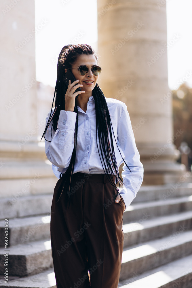 Fototapeta premium Young woman with braided hair walking downstairs of a beautiful architecture building and talking on the phone