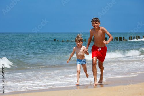 Brothers running alongside each other on the beach have fun