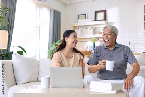 Lovely senior asian couple using a laptop together and having fun sitting on sofa at home.