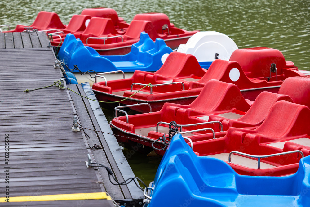 Red and blue pedalo parked on the pond next to the wooden jetty. Water recreation equipment ready for action