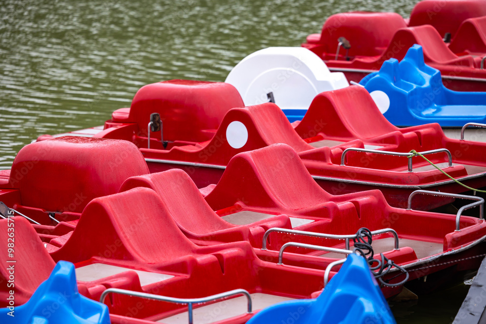 Red and blue pedalo parked on the pond next to the wooden jetty. Water recreation equipment ready for action