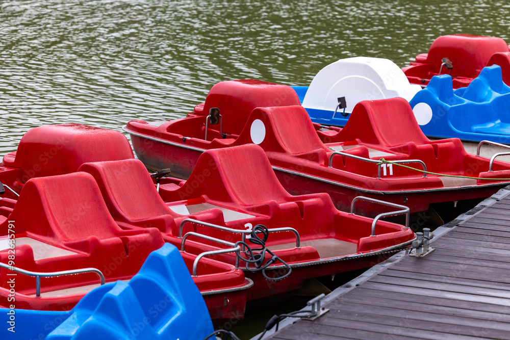 Red and blue pedalo parked on the pond next to the wooden jetty. Water recreation equipment ready for action