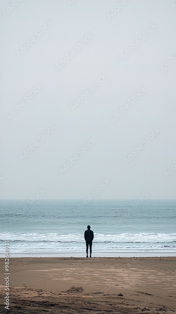 A solitary individual stands on a sandy beach facing the ocean, with a vast and cloudy sky overhead. The scene is minimalistic, with muted colors and a calm atmosphere. The waves of the ocean are gent A solitary individual stands on a sandy beach facing the ocean, with a vast and cloudy sky overhead. The scene is minimalistic, with muted colors and a calm atmosphere. The waves of the ocean are gent