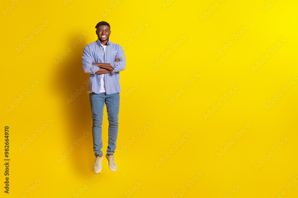 Full length photo of handsome good mood guy wear plaid shirt jumping high arms crossed emtpy space isolated yellow color background Full length photo of handsome good mood guy wear plaid shirt jumping high arms crossed emtpy space isolated yellow color background