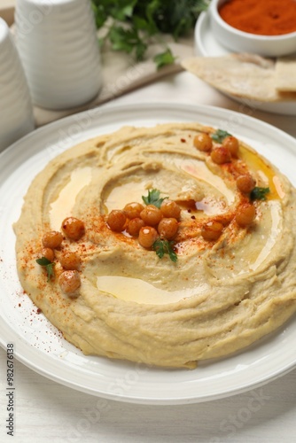 Delicious hummus with olive oil, chickpeas and paprika on white wooden table, closeup