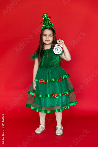 Happy child little girl in Christmas tree green costume with alarm clock. Christmas eve time. Holiday concept. New year time