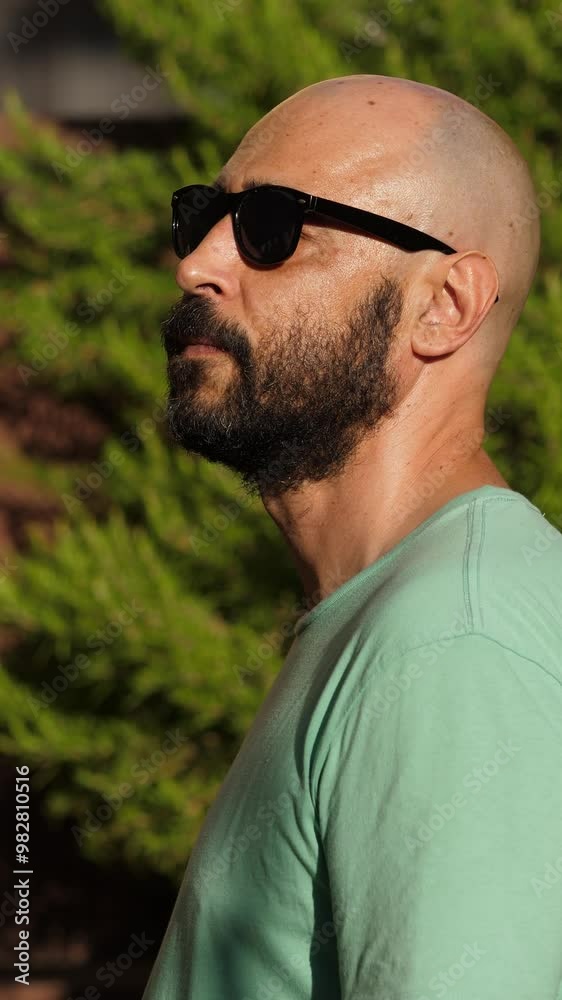 Vertical shot of a side view of a very thoughtful bald man wearing sunglasses. Captures a deep and contemplative mood. Vertical shot of a side view of a very thoughtful bald man wearing sunglasses. Captures a deep and contemplative mood.