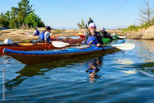 Photography Sea kayaker (young woman) in blue boat sits near rocky shore with friends  in Ge