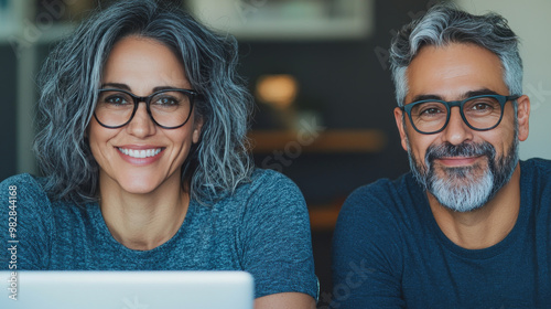 A smiling couple in glasses looks at the camera.