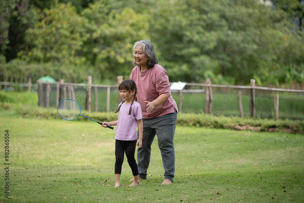 Fototapeta premium Happy Asian family children playing badminton with grandma in the park