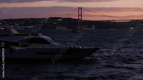 Twilight Voyage. Yacht Silhouette Against Red Illuminated Bridge in Istanbul photo