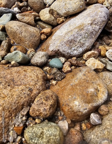 A serene beach scene featuring smooth pebbles and stones against a textured stone wall, capturing the natural beauty of gray and white hues along the shoreline