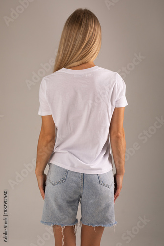 Blonde girl posing with her back on a white background in a white T-shirt and denim shorts