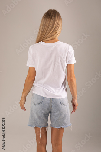 Fotografía Blonde girl posing with her back on a white background in a white T-shirt and de