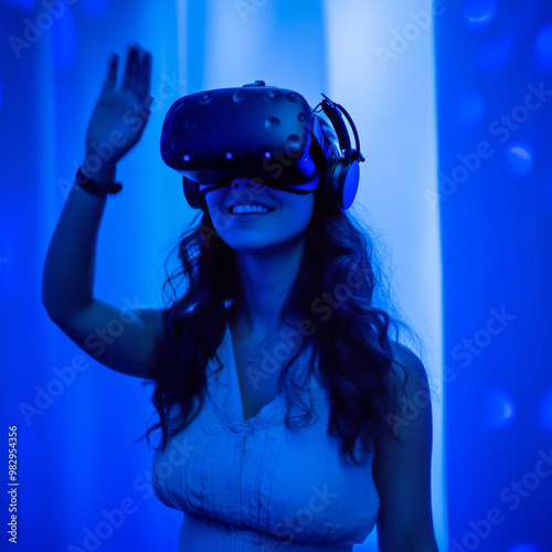 A woman wearing virtual reality headset waves her hand in blue lit environment, showcasing immersive experience of VR technology