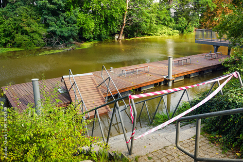 Wooden dock cordoned off with red and white striped caution tape, indicating potential flooding hazards. photo