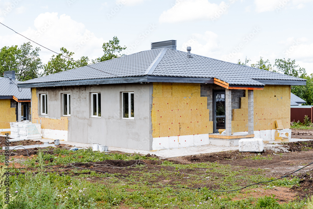 At this moment in time, a house is actively under construction in the very center of a stunning, expansive field, surrounded by vibrant green grass and the bright, clear blue sky above At this moment in time, a house is actively under construction in the very center of a stunning, expansive field, surrounded by vibrant green grass and the bright, clear blue sky above