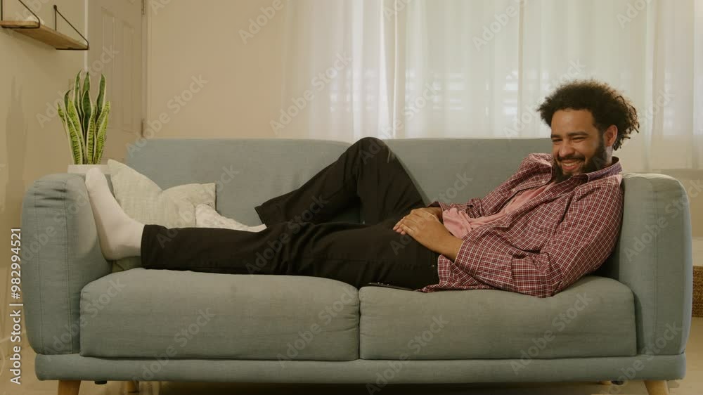 A young man is comfortably lounging on a soft and cozy sofa, smiling broadly with joy as he browses the vast internet on his mobile phone, savoring a delightful break from his work responsibilities A young man is comfortably lounging on a soft and cozy sofa, smiling broadly with joy as he browses the vast internet on his mobile phone, savoring a delightful break from his work responsibilities