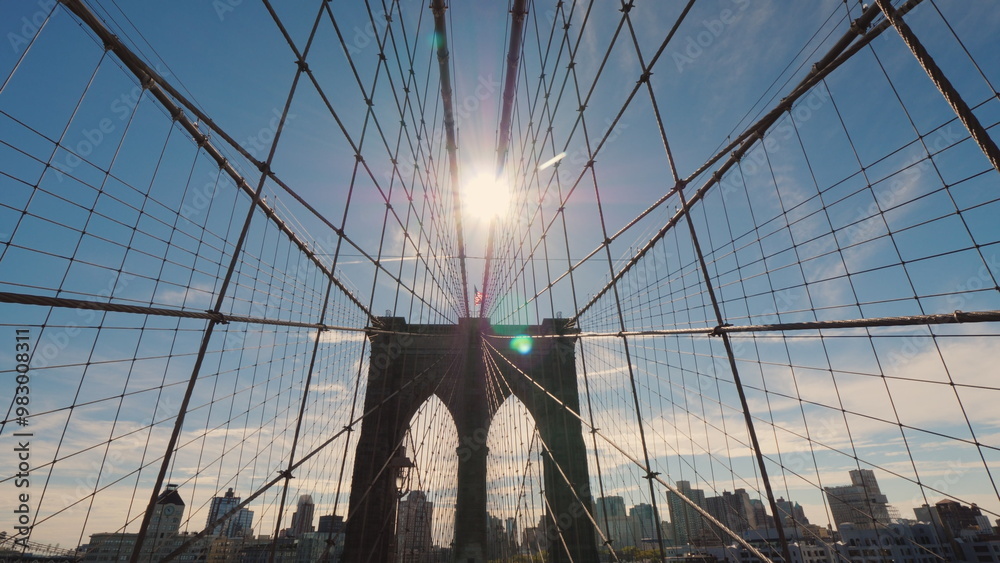 Obraz premium Brooklyn Bridge in the direction of Brooklyn. The sun high in the sky will light above the pillars of the bridge. Symbol of New York City