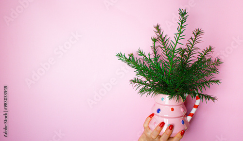 Womans hand is holding a christmas tree mug with branches, kitschy image on pink background