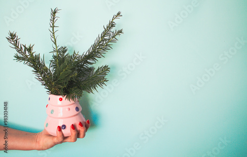 Unusual christmas postcard with womans hand holding a pink dotted mug with green branches on mint background
