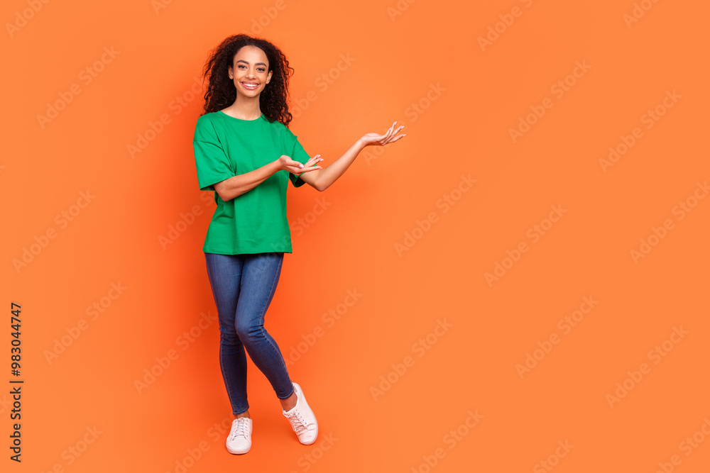 Photo of young funky attractive american girl wearing green casual t shirt two hands holding good deal isolated on orange color background Photo of young funky attractive american girl wearing green casual t shirt two hands holding good deal isolated on orange color background