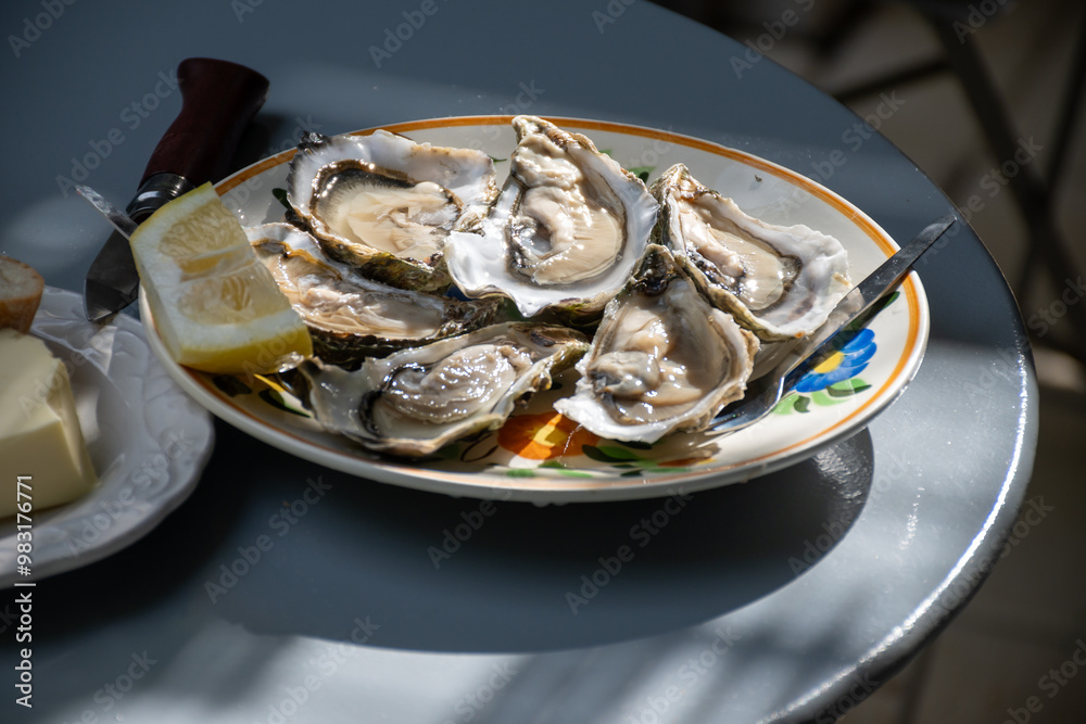 Plate with fresh live oysters with citron, bread, butter and white wine served at restaurant in oyster-farming village, Arcachon bay, Gujan-Mestras port, France Plate with fresh live oysters with citron, bread, butter and white wine served at restaurant in oyster-farming village, Arcachon bay, Gujan-Mestras port, France