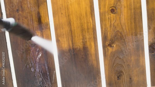 A close-up of a pressure washer spray head removing grime from a deck fence