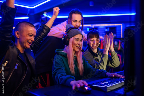 Gamer girl playing a video game in cybercafe while friends cheering. photo