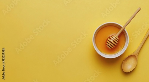 Natural honey in a bowl with a wooden dipper on a vibrant yellow background