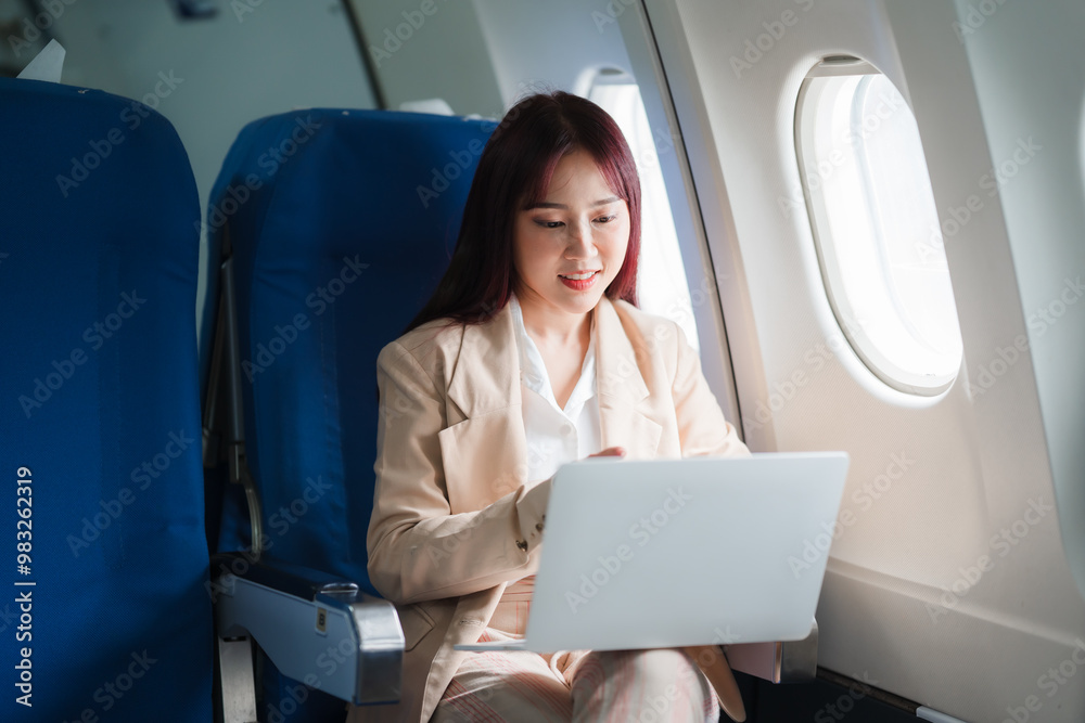 Businesswoman in the Clouds: A young Asian professional stays productive at 30,000 feet, working on her laptop with a warm smile during a flight. Businesswoman in the Clouds: A young Asian professional stays productive at 30,000 feet, working on her laptop with a warm smile during a flight.