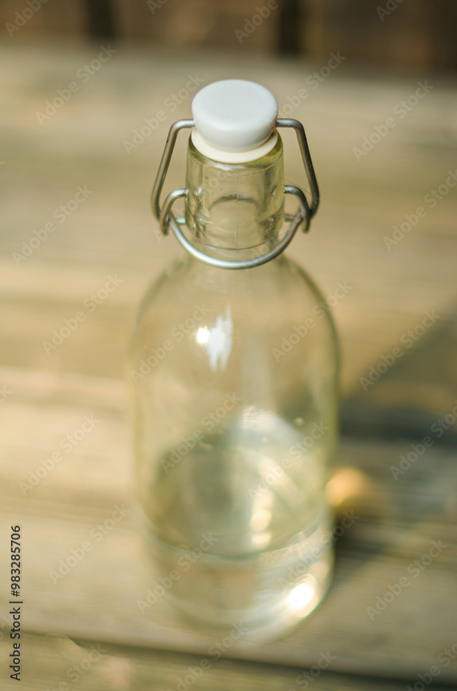 Close-up of a clear glass bottle with a metal swing-top lid, on a wooden surface. High quality photo Close-up of a clear glass bottle with a metal swing-top lid, on a wooden surface. High quality photo