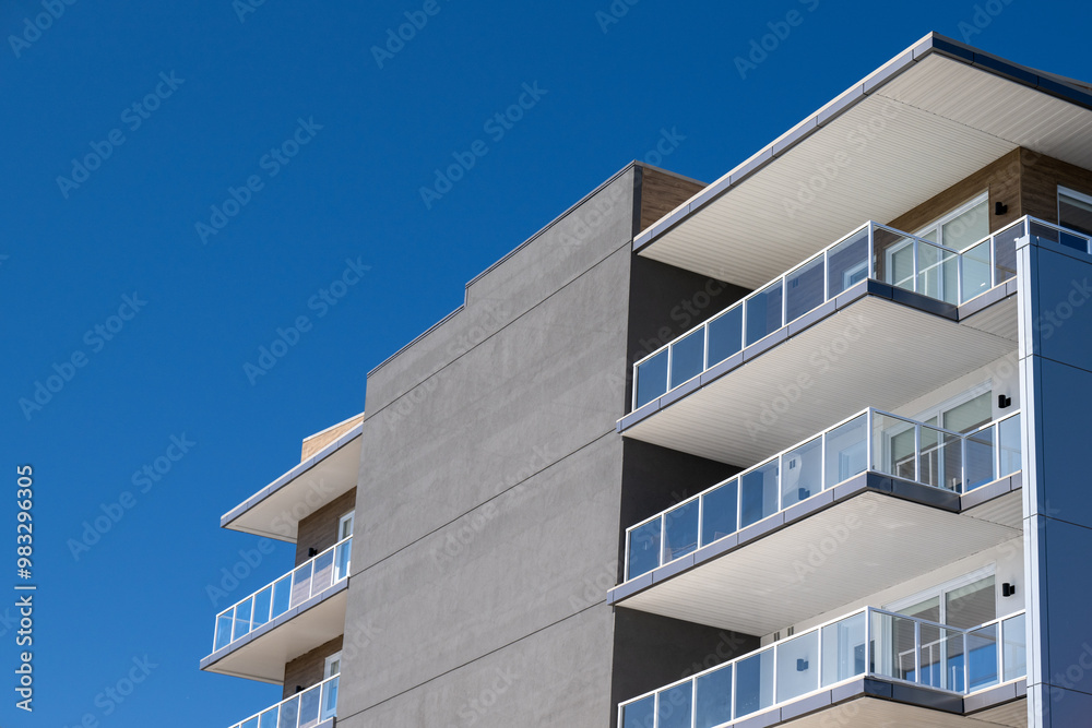 Corner view of a new apartment complex. The wall is grey modern metal paneling. Each unit has a glass balcony with a glass patio door. The condo units are on the corner of the modern style building. Corner view of a new apartment complex. The wall is grey modern metal paneling. Each unit has a glass balcony with a glass patio door. The condo units are on the corner of the modern style building.