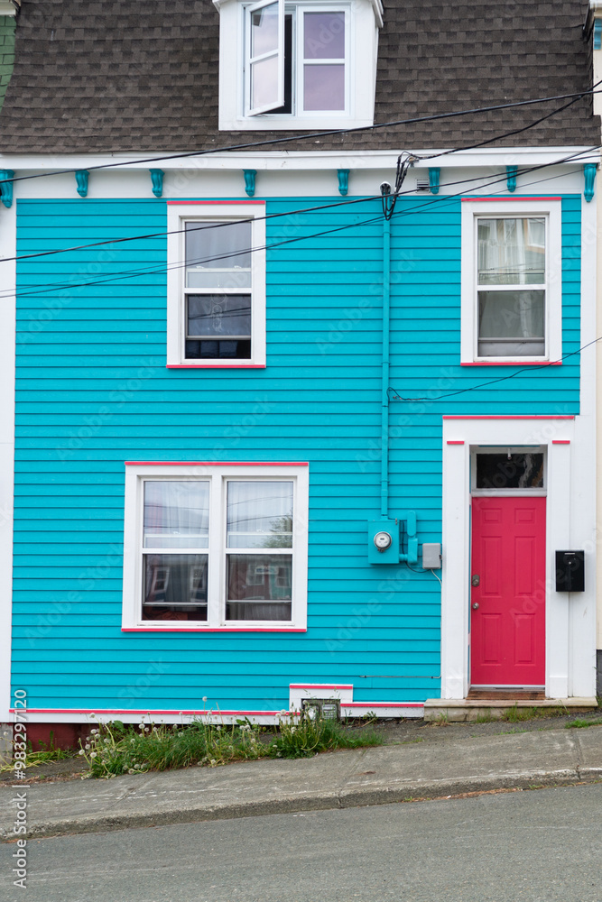 A bright teal blue historical wooden building with white trim, multiple glass windows, a colorful solid red door, a black mailbox with an asphalt mansard roof. There's an open window on the top floor. A bright teal blue historical wooden building with white trim, multiple glass windows, a colorful solid red door, a black mailbox with an asphalt mansard roof. There's an open window on the top floor.