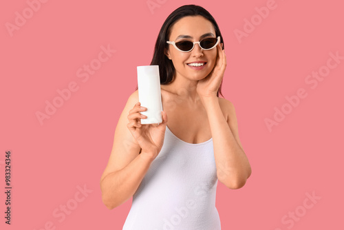 Young woman with sunscreen cream on pink background