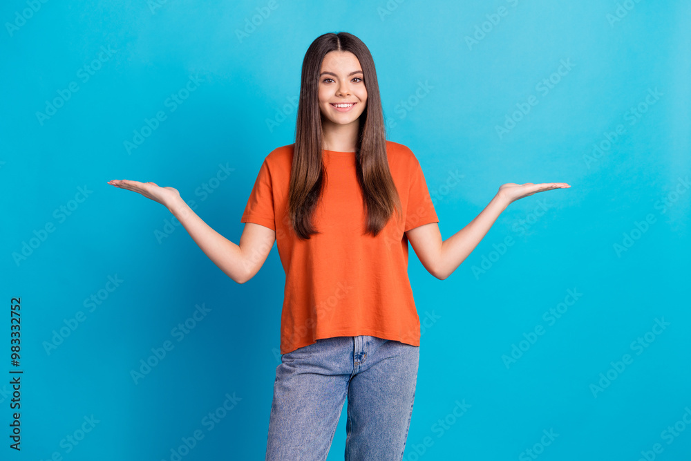 Photo portrait of lovely teen lady compare hold empty space dressed stylish orange garment isolated on blue color background Photo portrait of lovely teen lady compare hold empty space dressed stylish orange garment isolated on blue color background