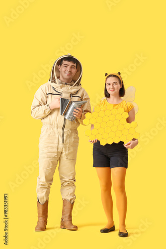 Male beekeeper with smoker and woman in bee costume on yellow background