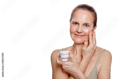 Elderly woman in her 60s with cream in her hand applying it to her face. Close-up portrait isolated on white background with space cut out for text