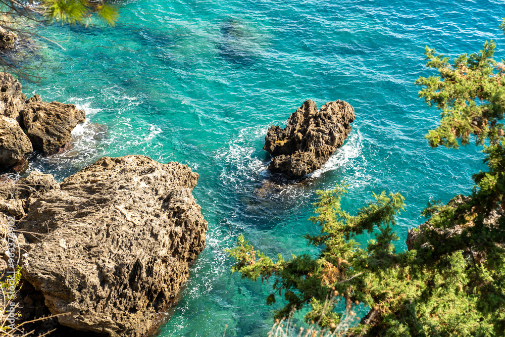 Obraz premium Sea waves hitting the high rocks in the deep blue sea and green vegetation