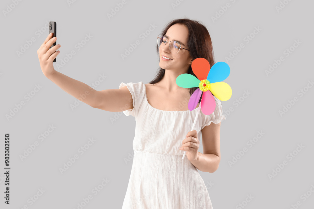 Young woman with toy windmill taking selfie on light background Young woman with toy windmill taking selfie on light background