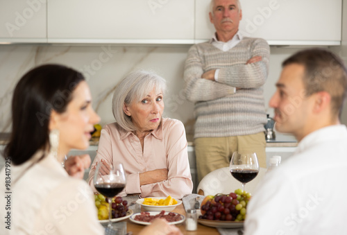 Young girl coquetting in a free manner with man around the table in front of elderly parents who demonstrate disagreeable attitude photo