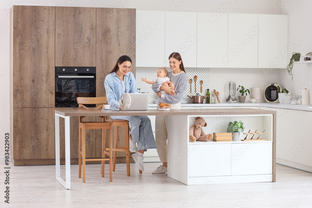 Young lesbian couple with their little baby using laptop in kitchen Young lesbian couple with their little baby using laptop in kitchen
