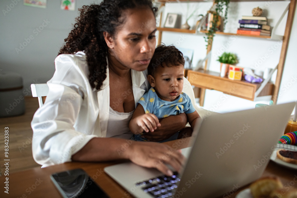 Mother working on laptop while watching toddler son at home Mother working on laptop while watching toddler son at home