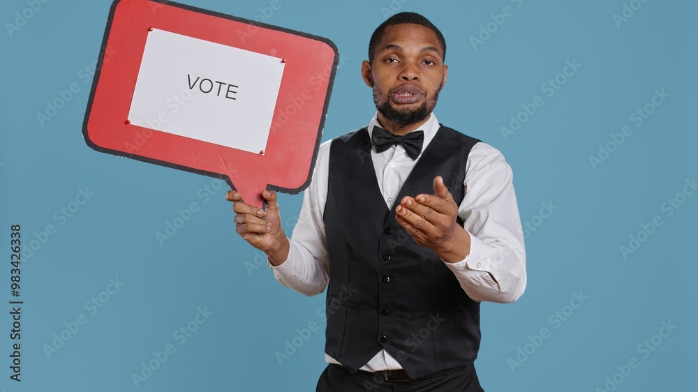 Hospitality industry worker shows speech bubble with political message, urging people to vote with cardboard sign advertisement. Hotel porter employee holds icon with commercial ad. Camera B. Hospitality industry worker shows speech bubble with political message, urging people to vote with cardboard sign advertisement. Hotel porter employee holds icon with commercial ad. Camera B.