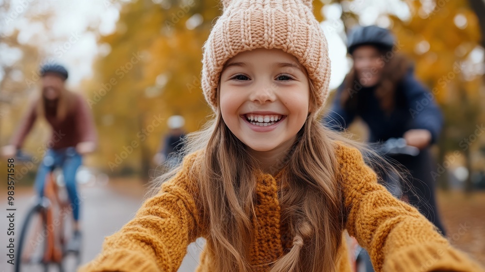 A joyful little girl wearing a knit hat and sweater pedals her bike happily, surrounded by family in a vibrant autumn setting full of golden leaves. A joyful little girl wearing a knit hat and sweater pedals her bike happily, surrounded by family in a vibrant autumn setting full of golden leaves.
