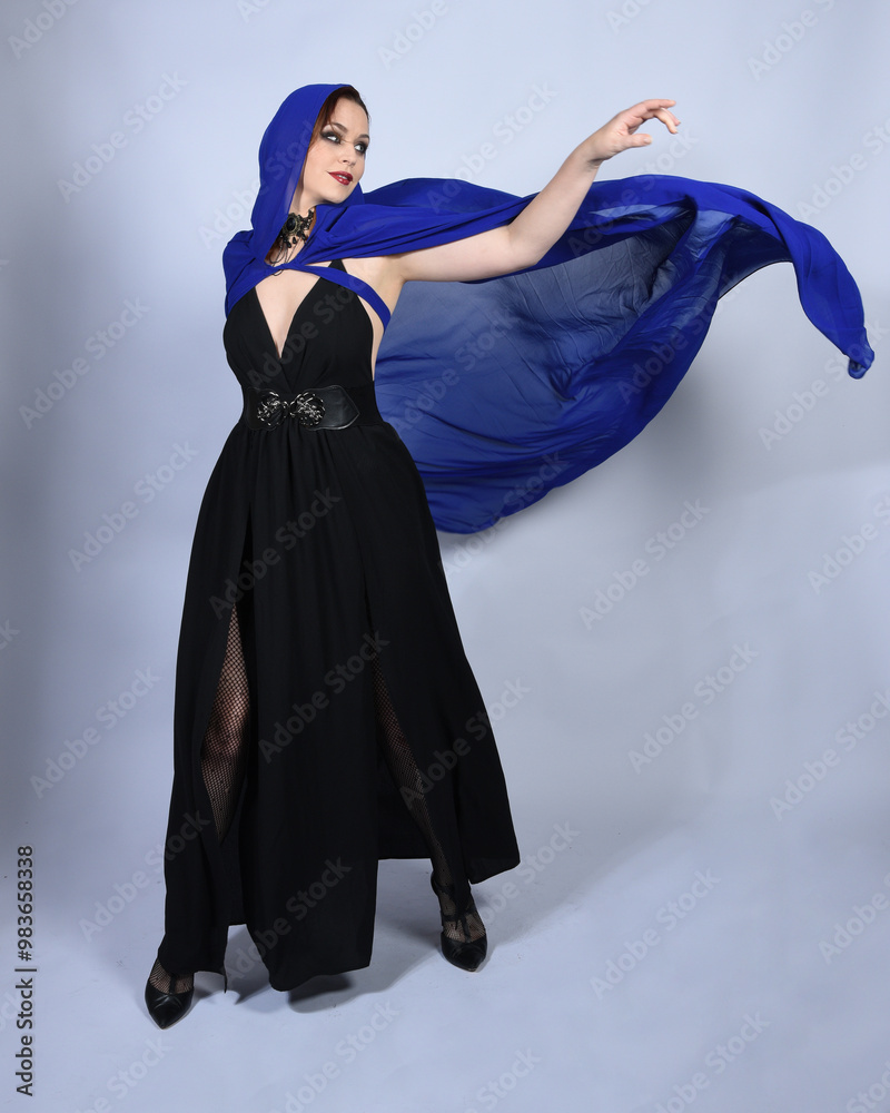 Φωτογραφία Full length portrait of  female red head model wearing  glamorous black witch dress with blue fantasy cloak halloween costume