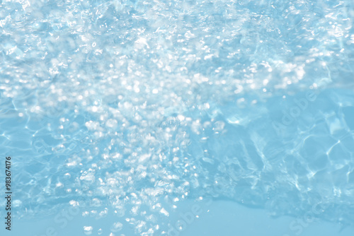 Blue water with ripples on the surface. Defocus blurred transparent blue colored clear calm water surface texture with splashes and bubbles. Water waves with shining pattern texture background.