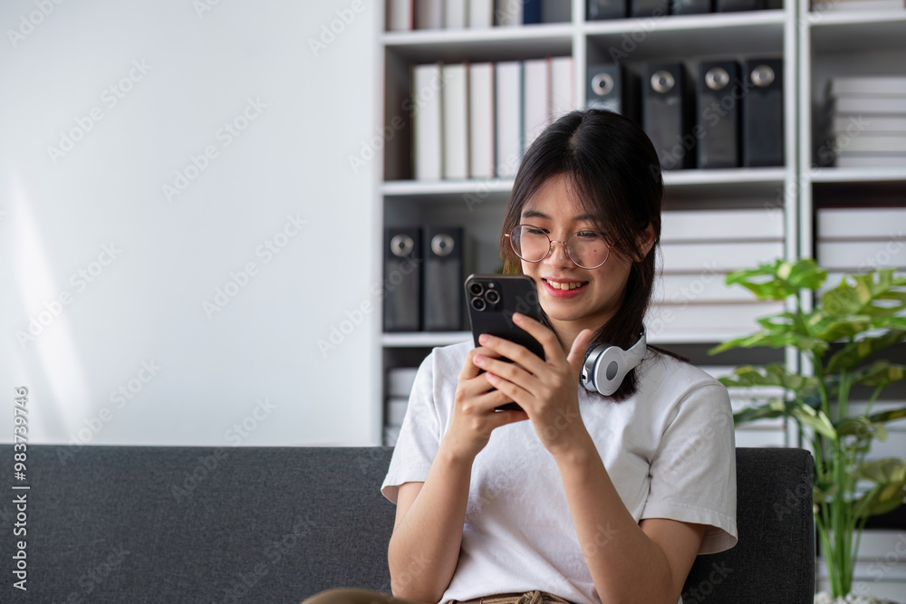 Young Woman Relaxing on Sofa, Enjoying Music and Playing on Phone in Modern Living Room Young Woman Relaxing on Sofa, Enjoying Music and Playing on Phone in Modern Living Room