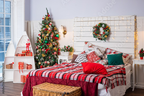 Interior of festive bedroom with comfortable bed and Christmas tree. checkered blanket. Christmas home decoration. Christmas tree, garland with lights, gifts. Winter holidays