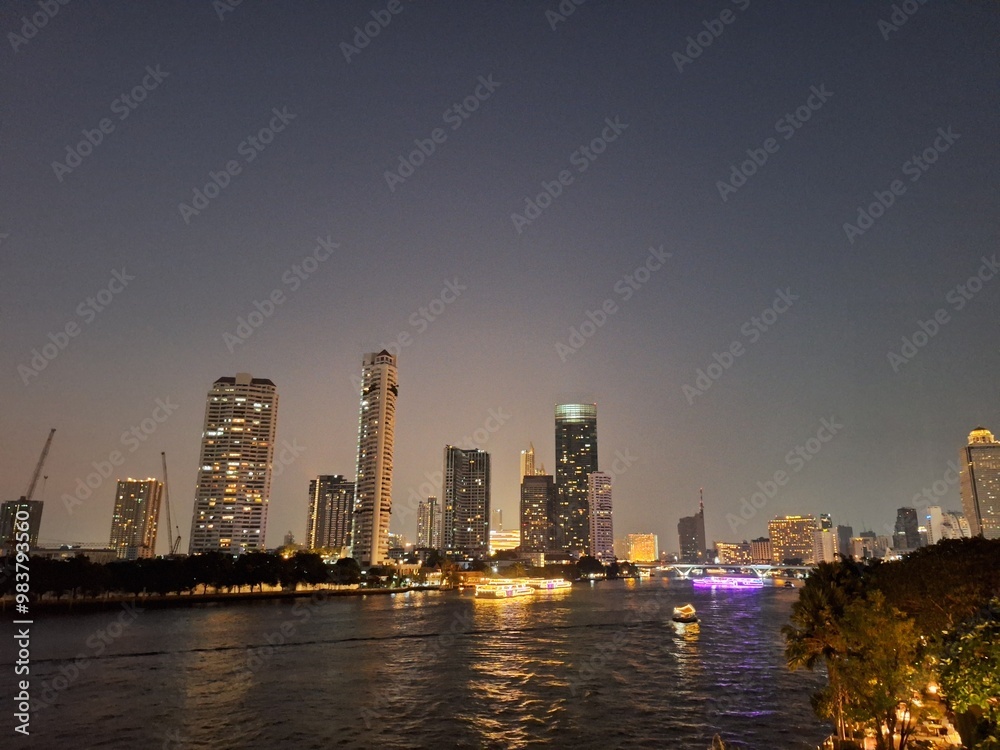 Nighttime scene of tall buildings adorned with lights by the riverside. Perfect for use as an illustration element or as a background Nighttime scene of tall buildings adorned with lights by the riverside. Perfect for use as an illustration element or as a background